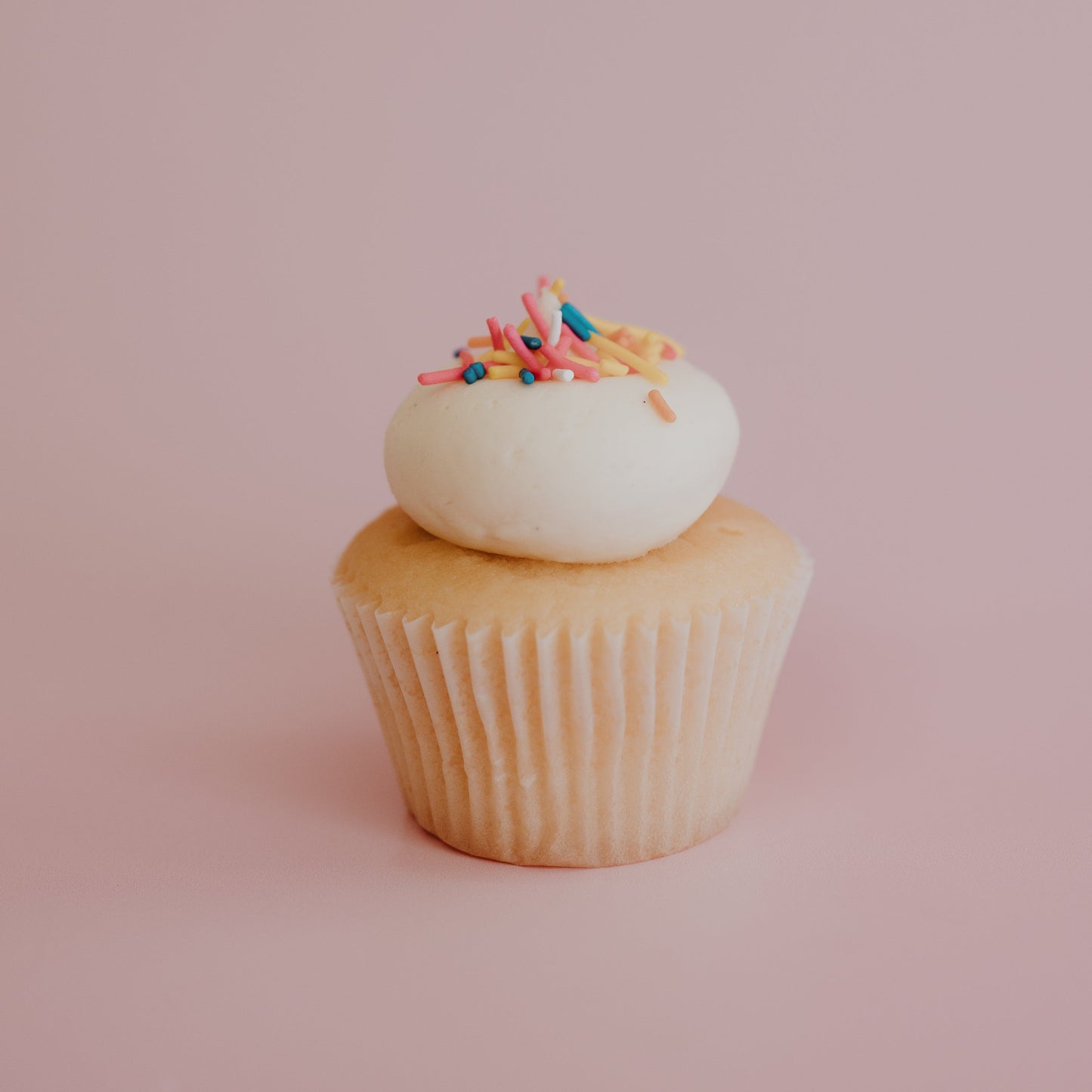 Cupcake with white frosting and colorful sprinkles on a pink background