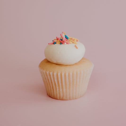 Cupcake with white frosting and colorful sprinkles on a pink background